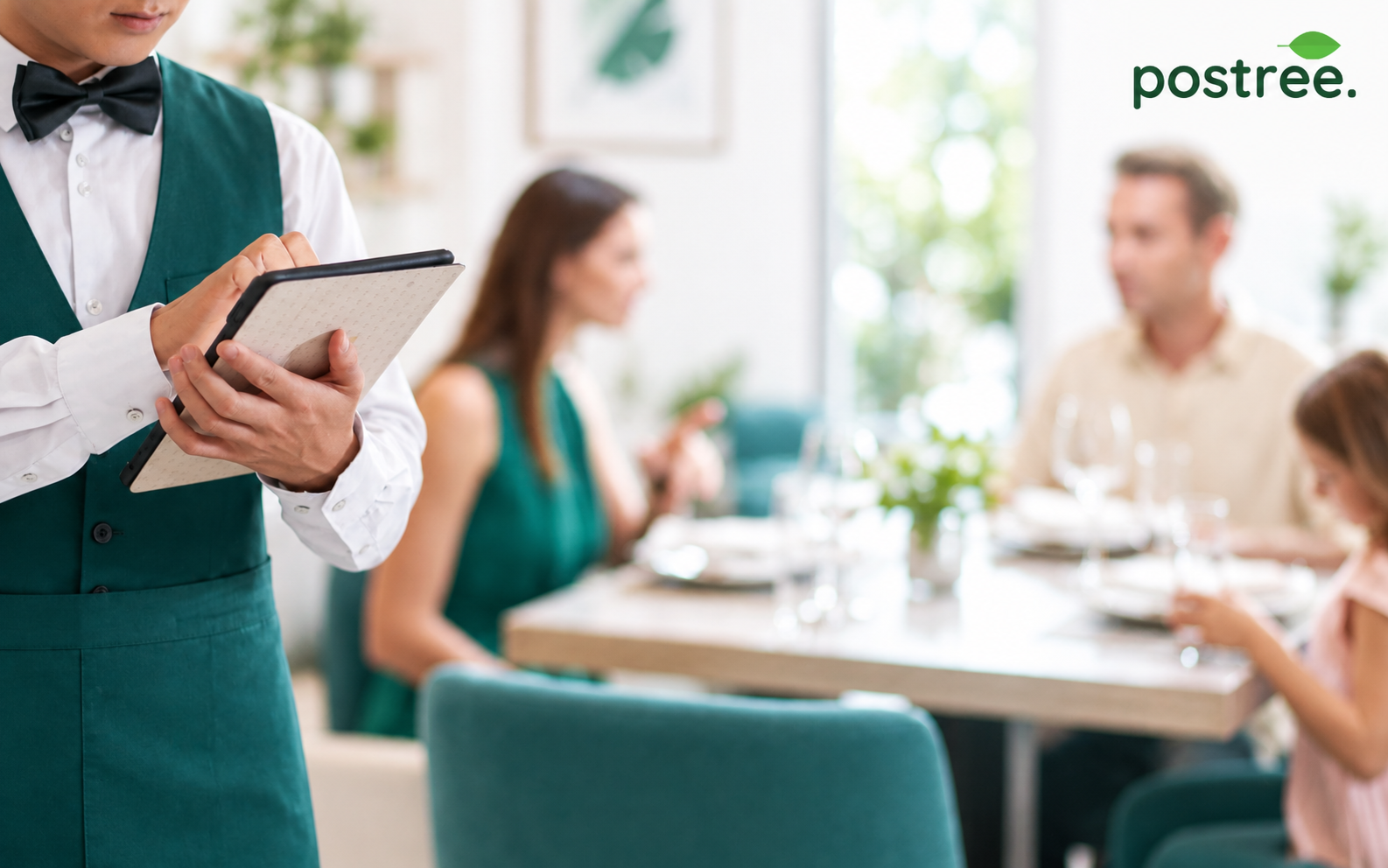 A waiter taking a booking on a handheld device from guests seated at a table in a warm restaurant
